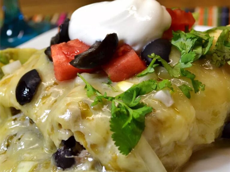 Close up view of homemade chicken enchiladas with tomatoes, black olives, fresh herbs and sour cream on a plate