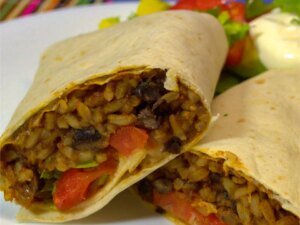 Close up view of a black bean and rice burrito served with salad on a white plate