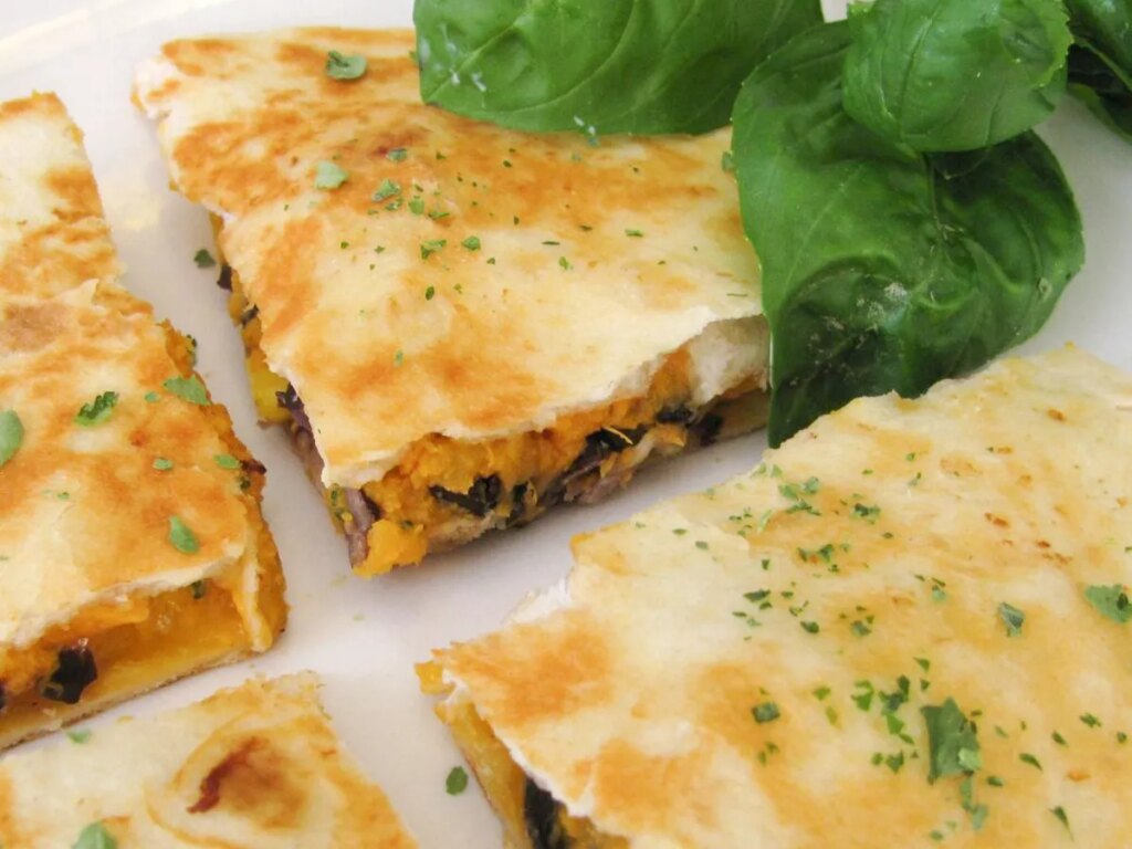 Close up view of black bean and sweet potato quesadillas garnished with fresh herbs on a white plate