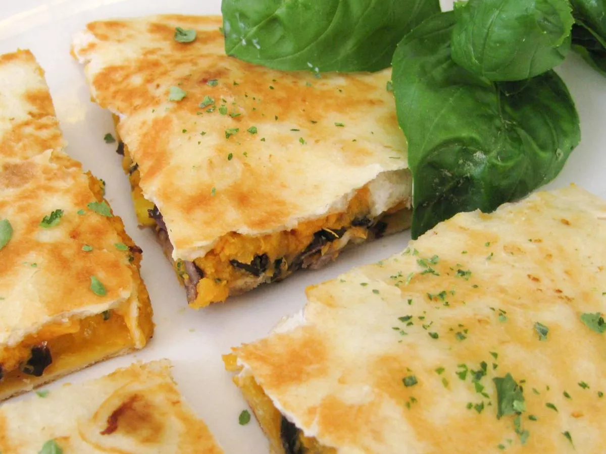 Close up view of black bean and sweet potato quesadillas garnished with fresh herbs on a white plate