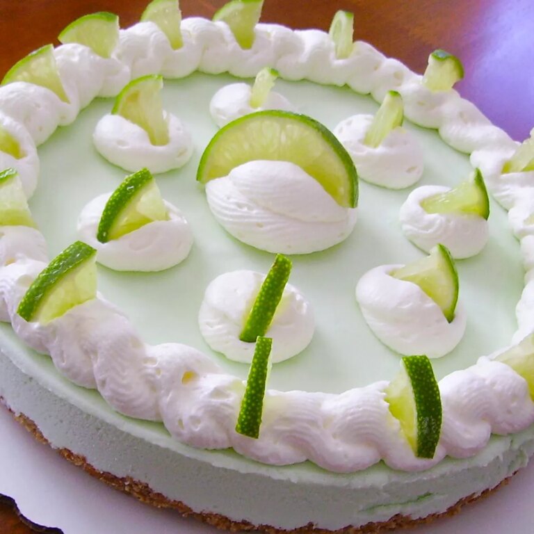 Close up view of a frozen margarita pie garnished with white icing and lime slices on a white platter