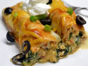 Close up view of spinach and chicken enchiladas garnished with sour cream, green onions and black olives on a white plate