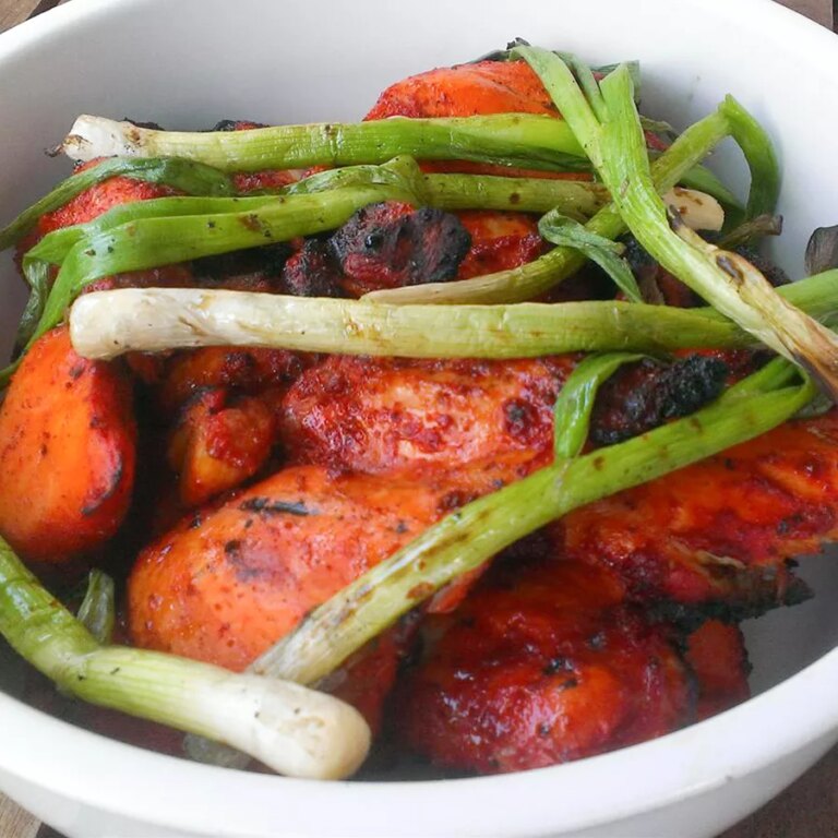 Close up view of tandoori chicken with green onions in a white bowl