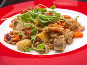 Close up view of baingan bharta (eggplant curry) garnished with fresh herbs on a red and white plate