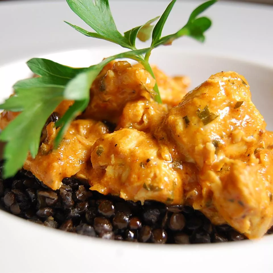 close up view of Chicken Tikka Masala with fresh herbs over black grains in a white bowl