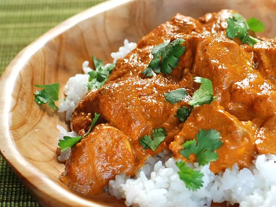 Close up view of punjabi chicken in thick gravy on white rice, garnished with fresh herbs, in a wooden bowl