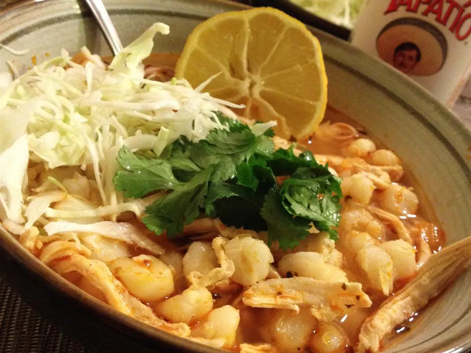 Close up view of easy chicken posole in a bowl, garnished with herbs and lemon