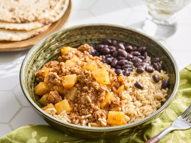 Mexican picadillo served with rice, black beans, and tortillas in the background.