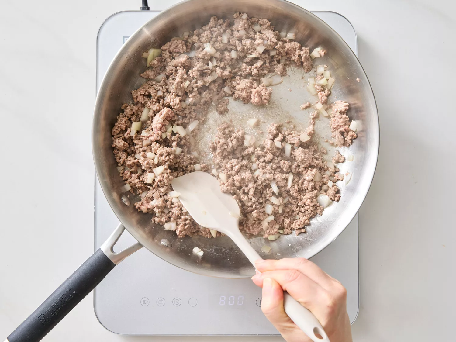 Ground beef and onions cooking in a skillet, hand stirring with a spatula.