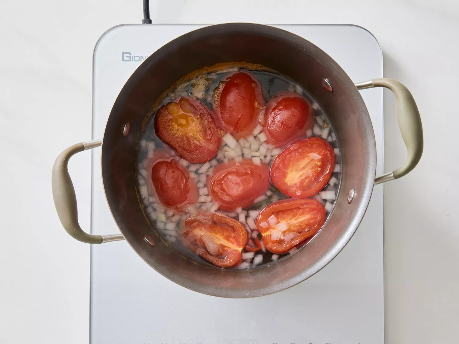 Tomatoes and chopped onions simmering in water inside a pot on a stovetop.