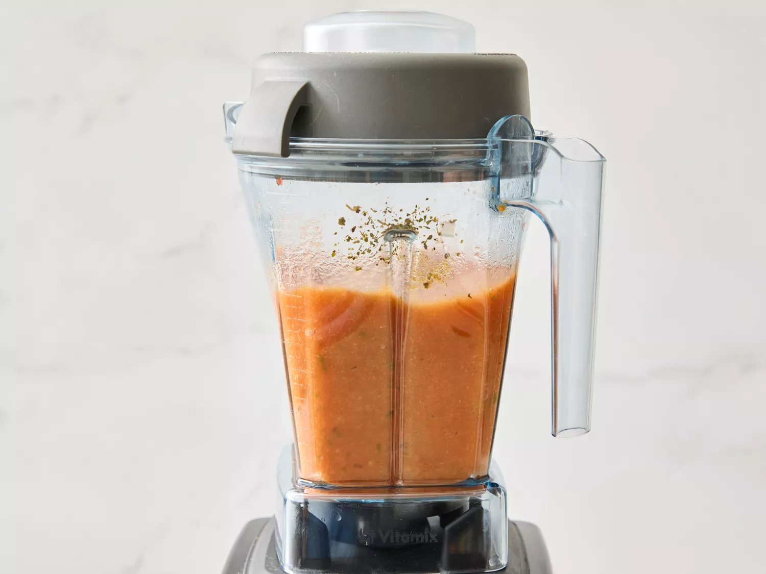 Blender with orange sauce and spices inside, part of a recipe preparation.