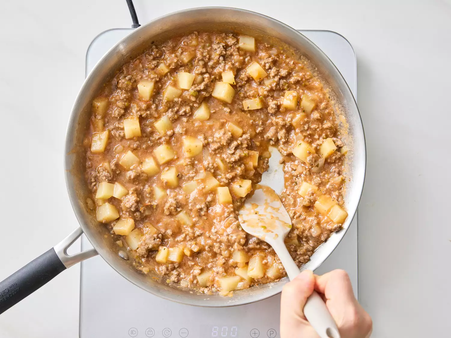 Cooking ground meat and diced potatoes in a skillet, stirred with a spatula.