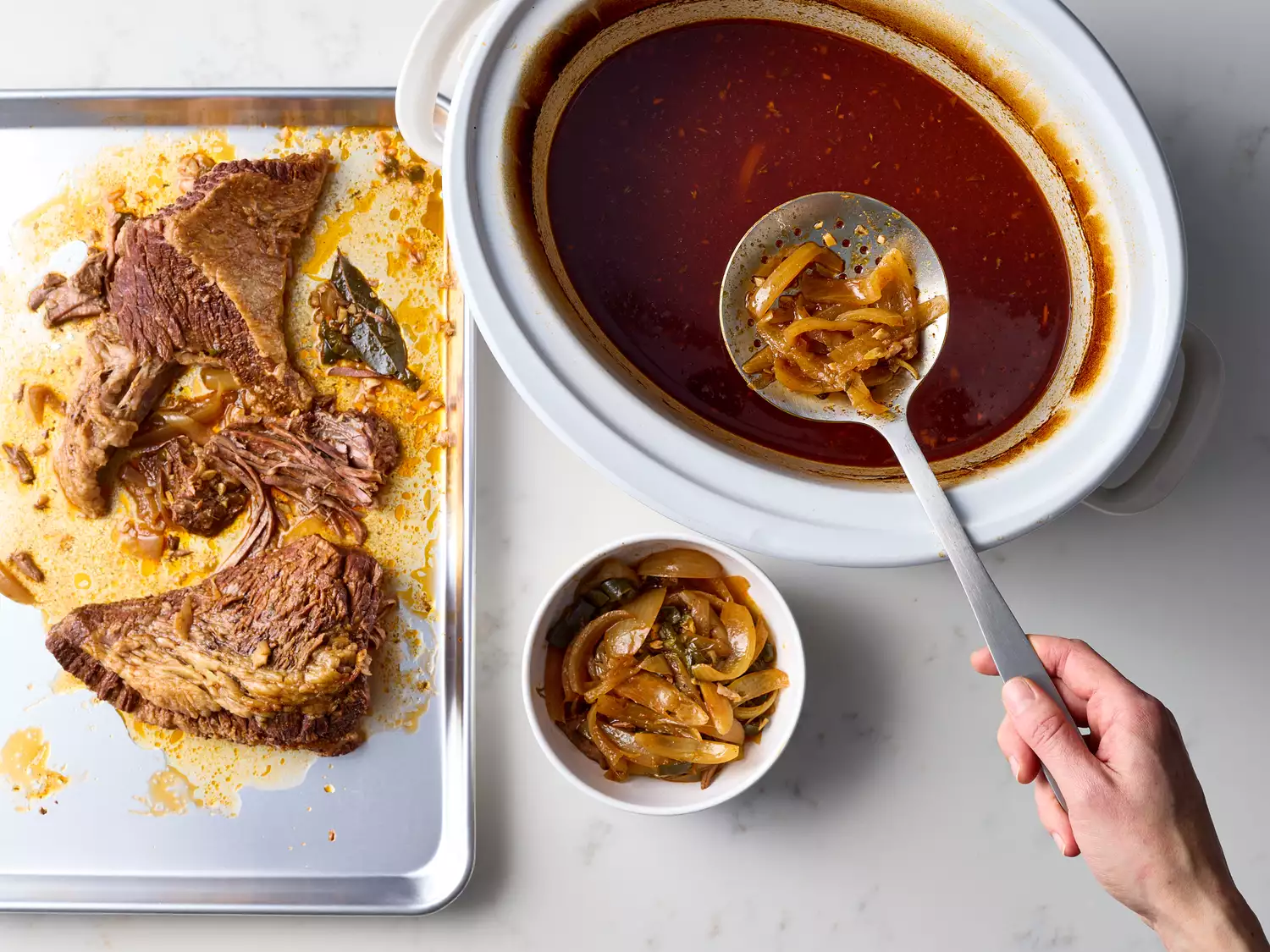 Brisket on a baking tray and onions being moved with a spoon from a slow cooker to a bowl 