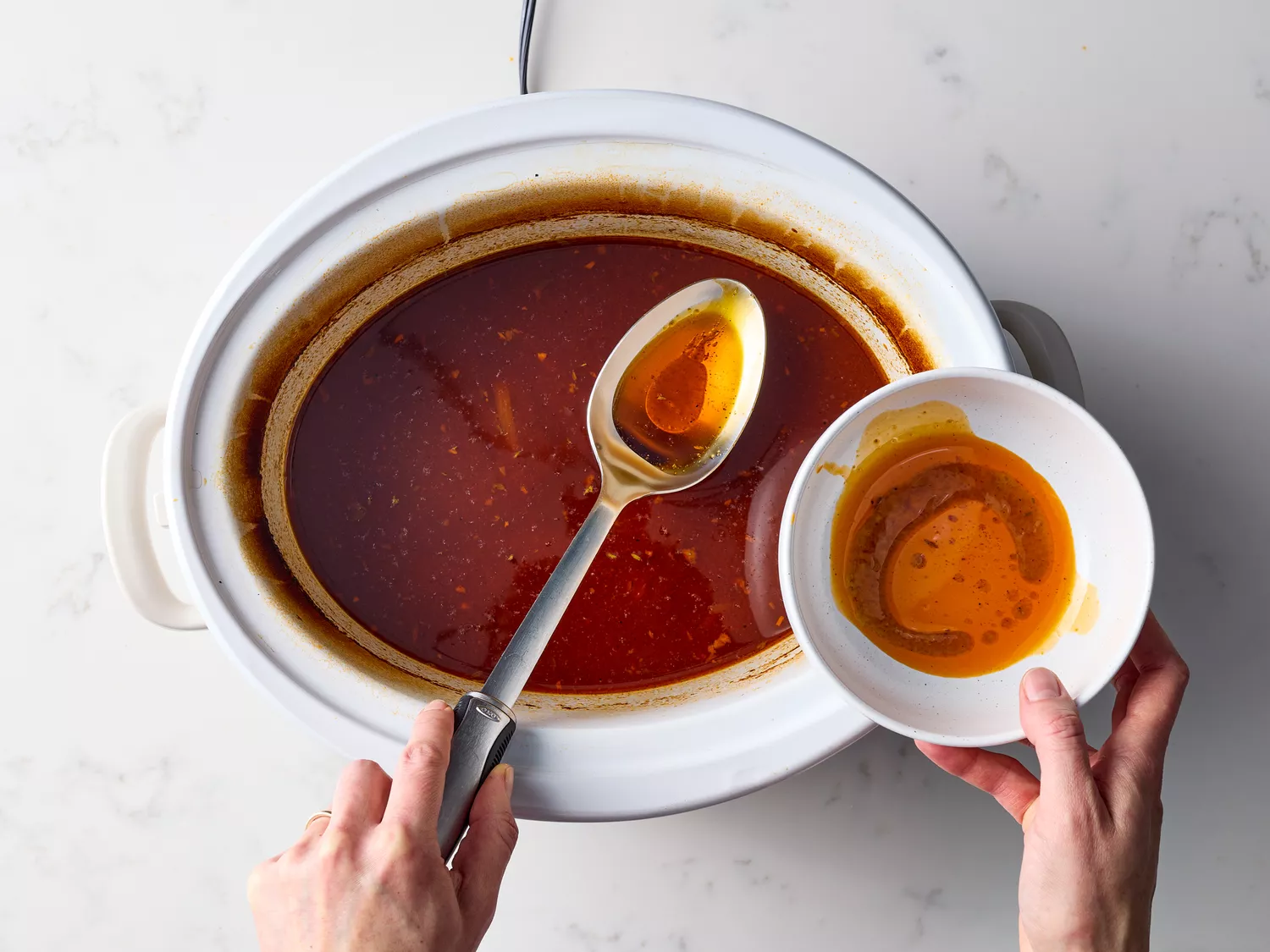 Spoon removing excess fat from slow cooker broth