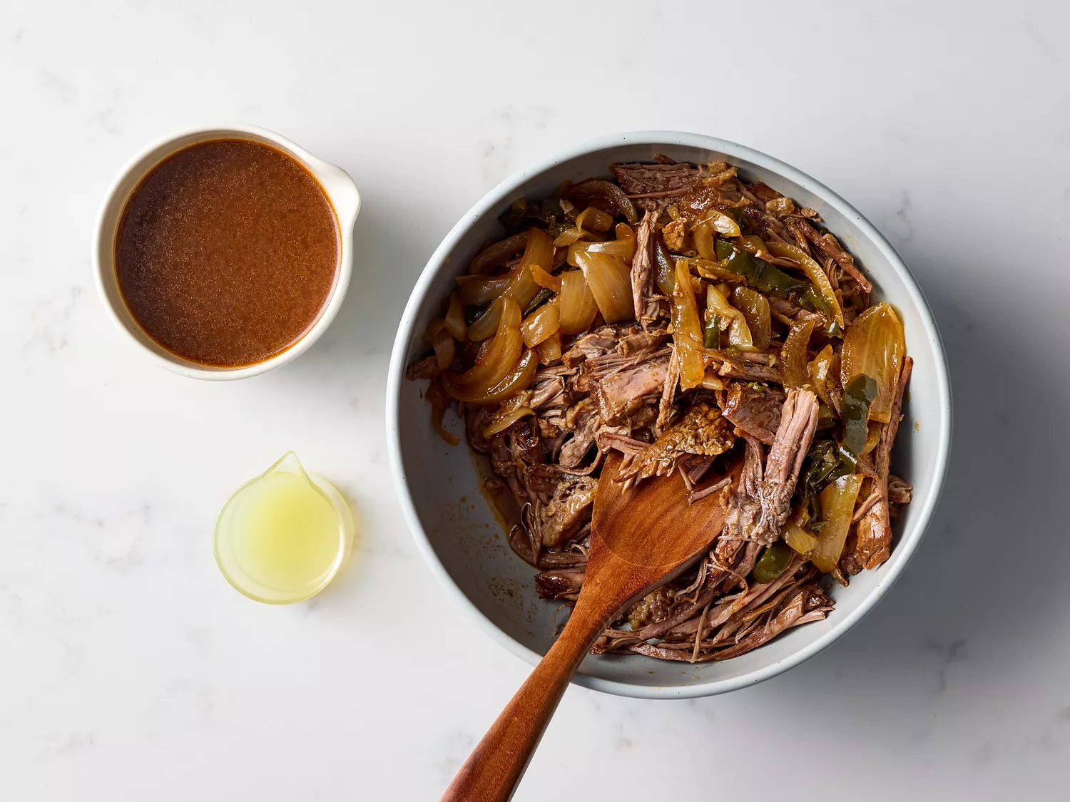 Shredded brisket mixed with onions in a serving bowl next to lime juice and sauce 