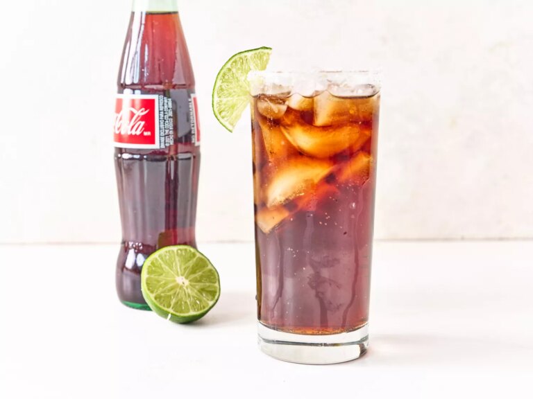 Batanga cocktail in a glass garnished with a lime wedge, next to a bottle of mexican coca cola and half a lime
