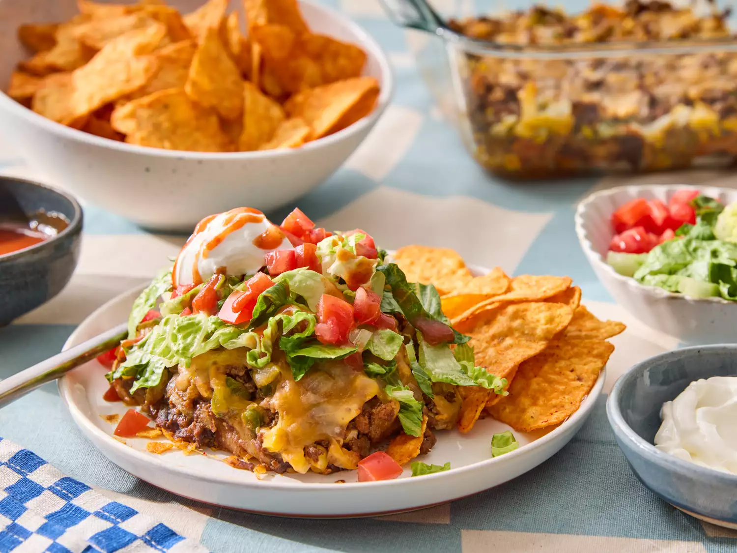 Taco salad casserole served on a plate with tortilla chips and toppings, surrounded by various dishes and condiments