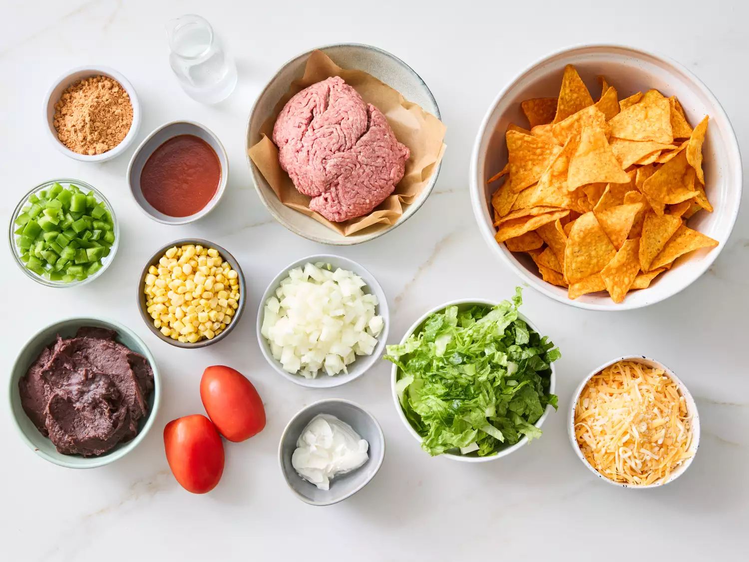 Ingredients laid out for taco salad casserole including meat, tortilla chips, and vegetables