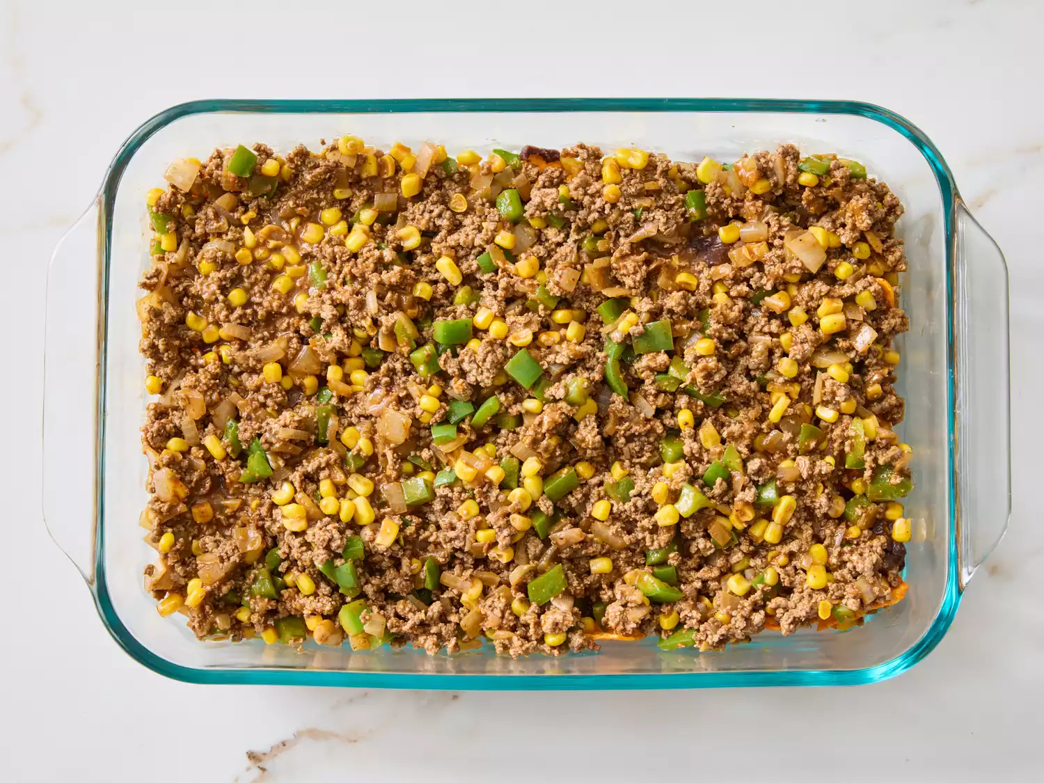 Baked taco salad casserole in a glass dish, showing mixed ground beef and vegetables