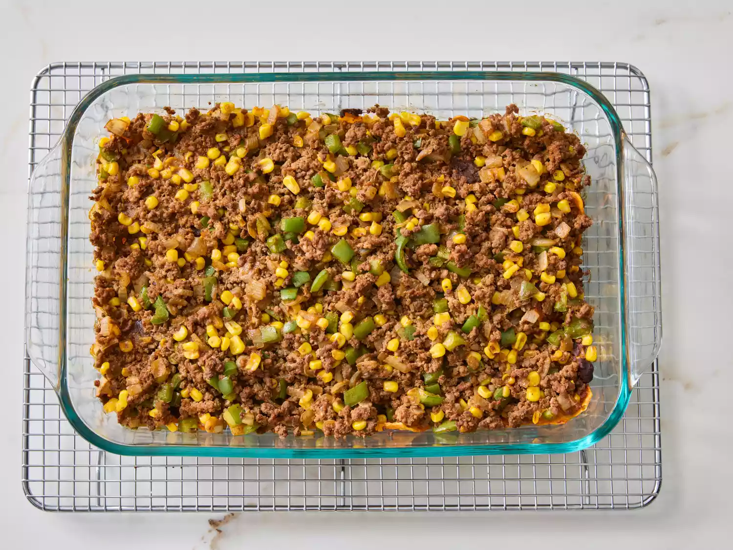 Glass dish containing taco salad casserole with meat, corn, and vegetables on a cooling rack