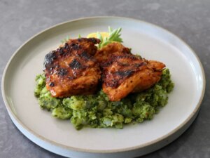 Rimmed white plate with herbed mashed potatoes topped with grilled chicken thighs