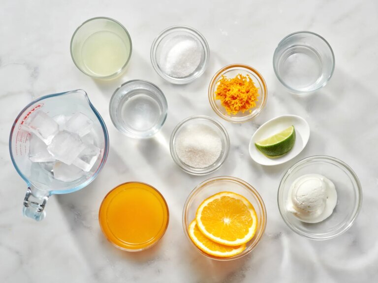 Ingredients for making an orange creamsicle margarita on a marble surface in separate containers