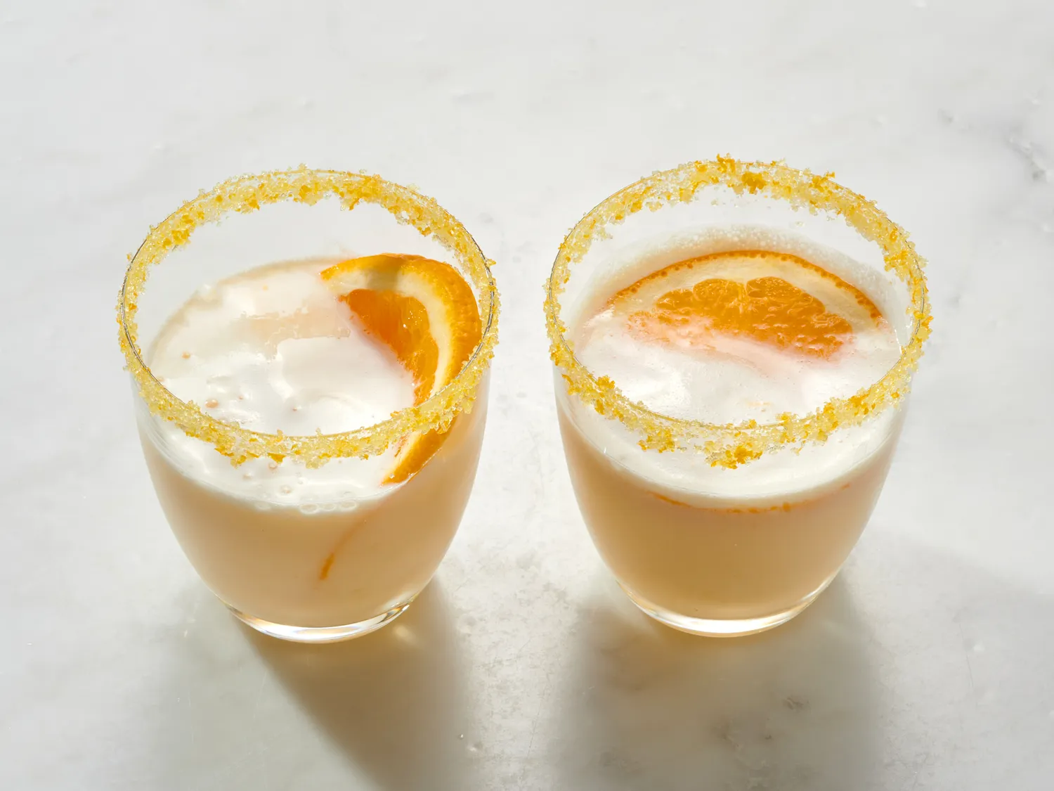 Two Orange Creamsicle Margaritas in glasses with sugar rims, filled with a creamy orange cocktail with orange slices resting on the sides
