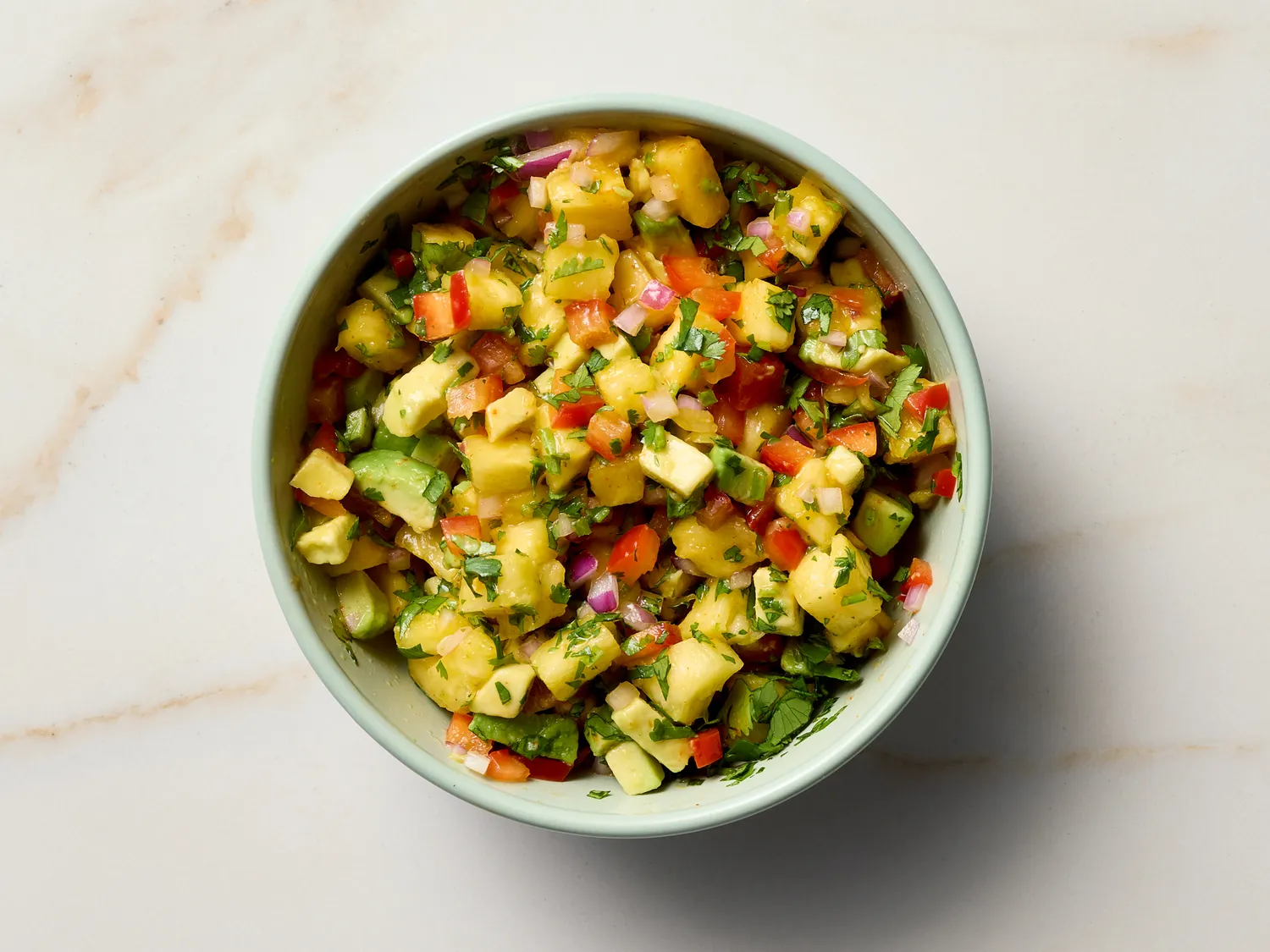 A bowl of salsa with diced fruits, vegetables, and herbs