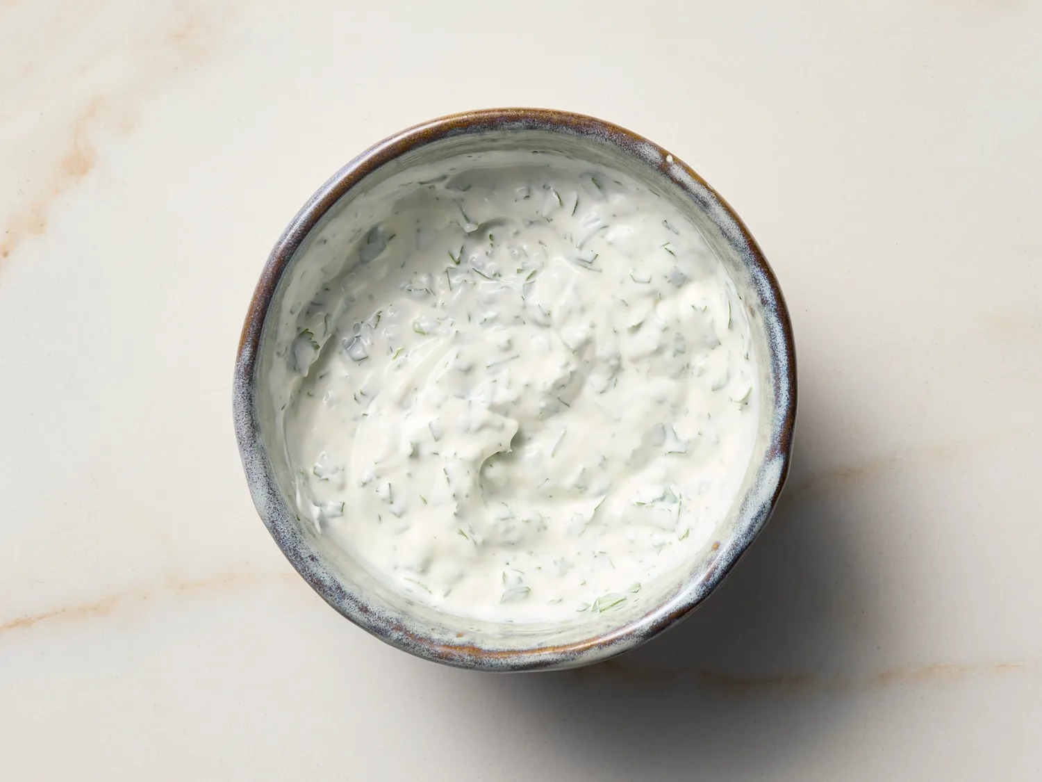A bowl of creamy sauce with visible herbs