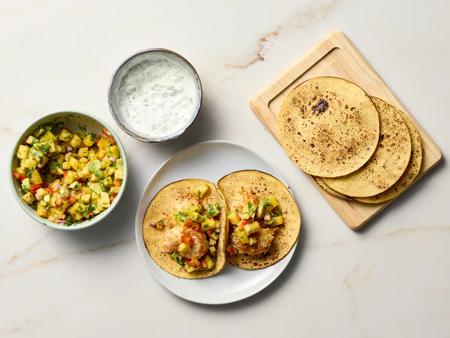 Crispy shrimp tacos served with a bowl of salsa and a creamy dip, tortillas placed on a wooden cutting board in the background