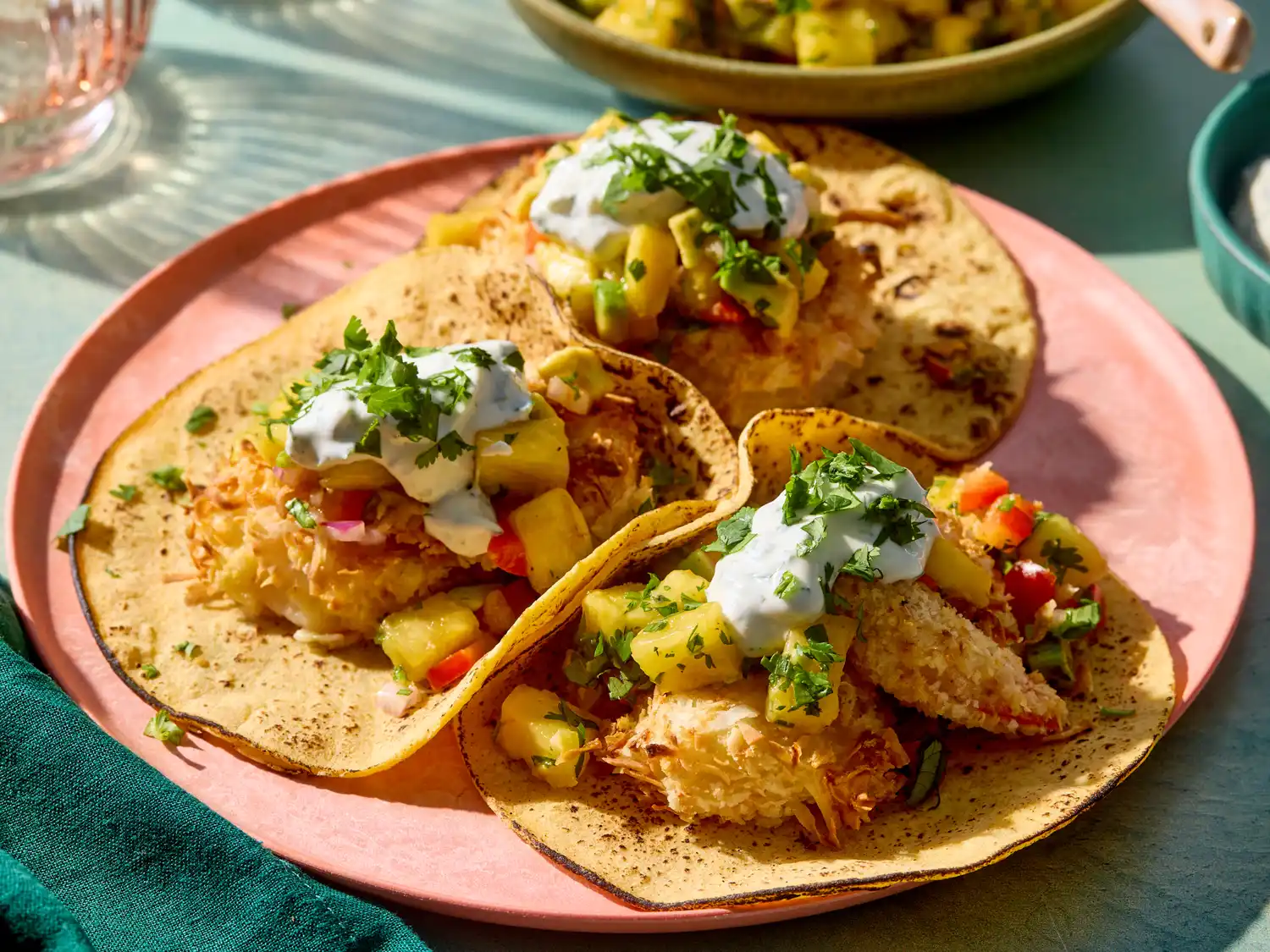 Three crisp coconut shrimp tacos garnished with pineapple salsa and drizzled with a creamy topping on a plate