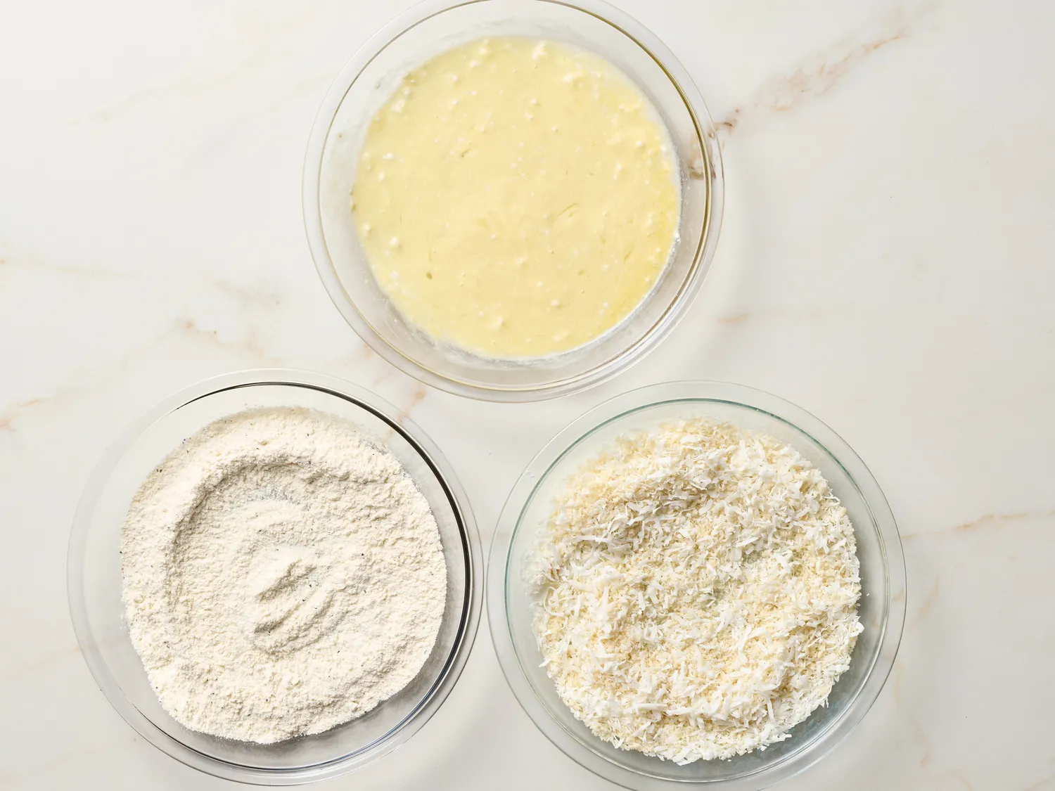 Three bowls with flour, batter, and shredded coconut, part of a recipe preparation step for coconut shrimp tacos