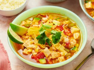 Bowl of chicken tortilla soup with lime wedges and cilantro garnish, surrounded by culinary items