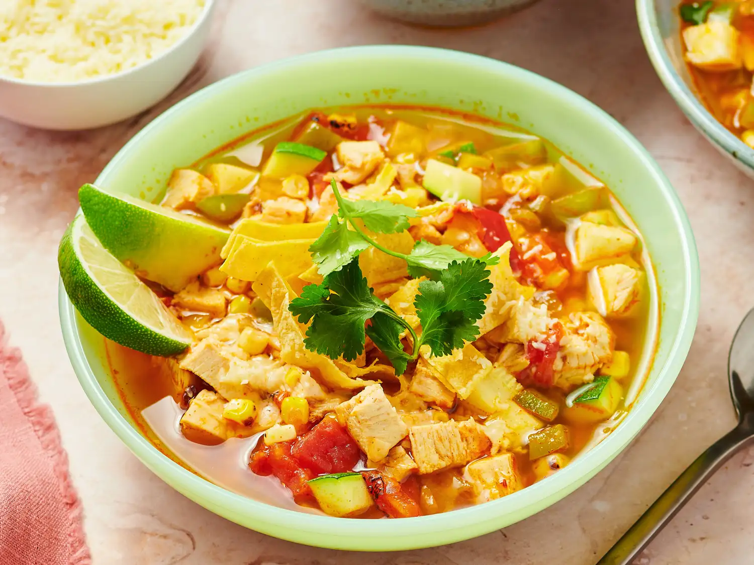 Bowl of chicken tortilla soup with lime wedges and cilantro garnish, surrounded by culinary items