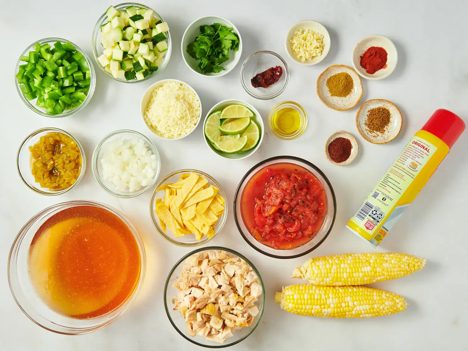 Ingredients arranged for making chicken tortilla soup, including vegetables, broth, spices, and canned tomatoes
