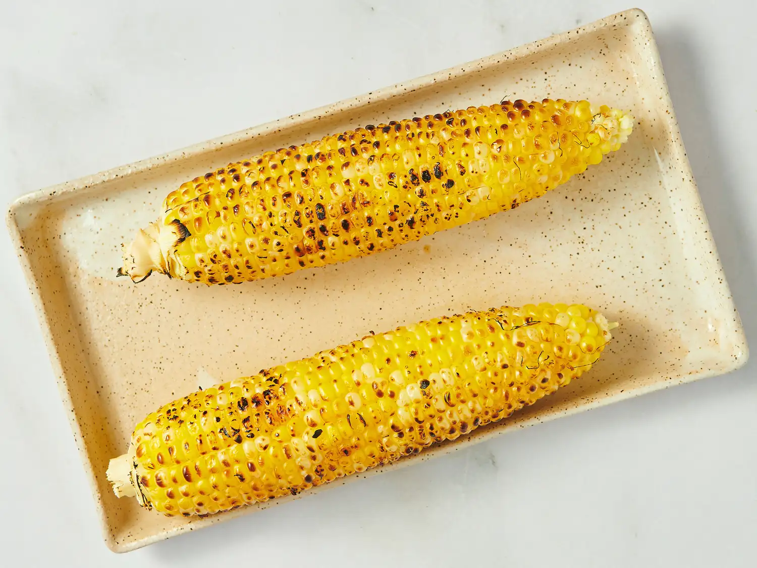 Two charred corn ears on a rectangular plate