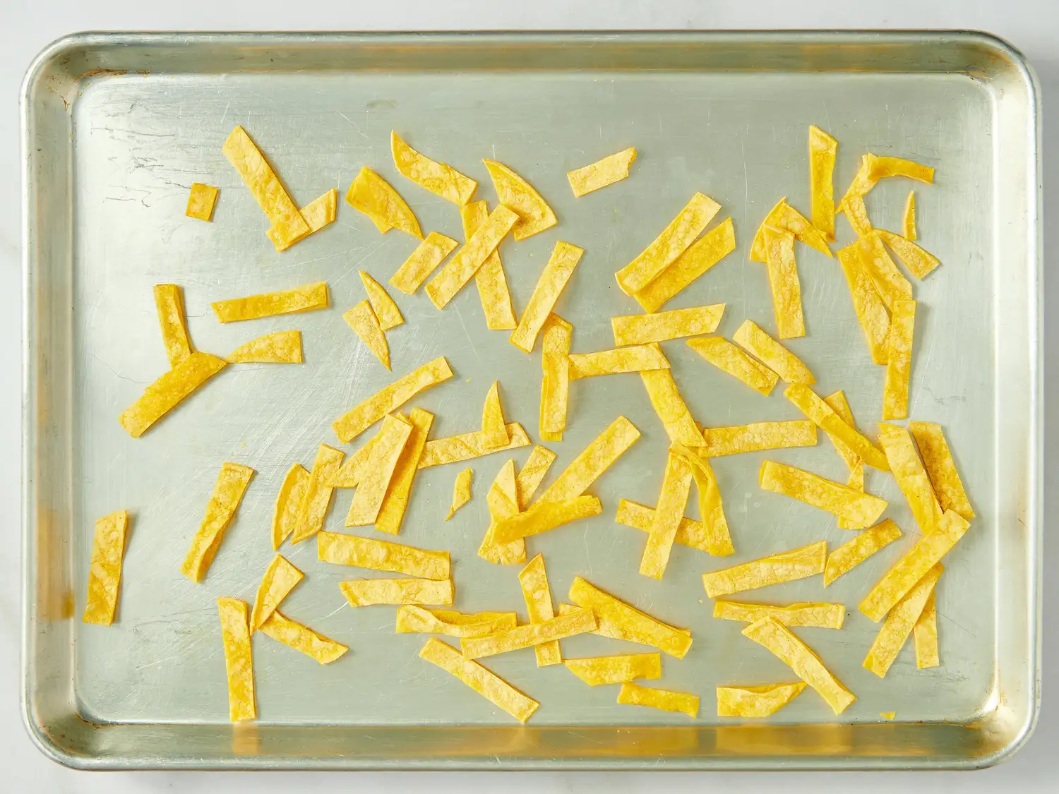 Tortilla strips spread on a baking sheet, prepared for baking or cooking