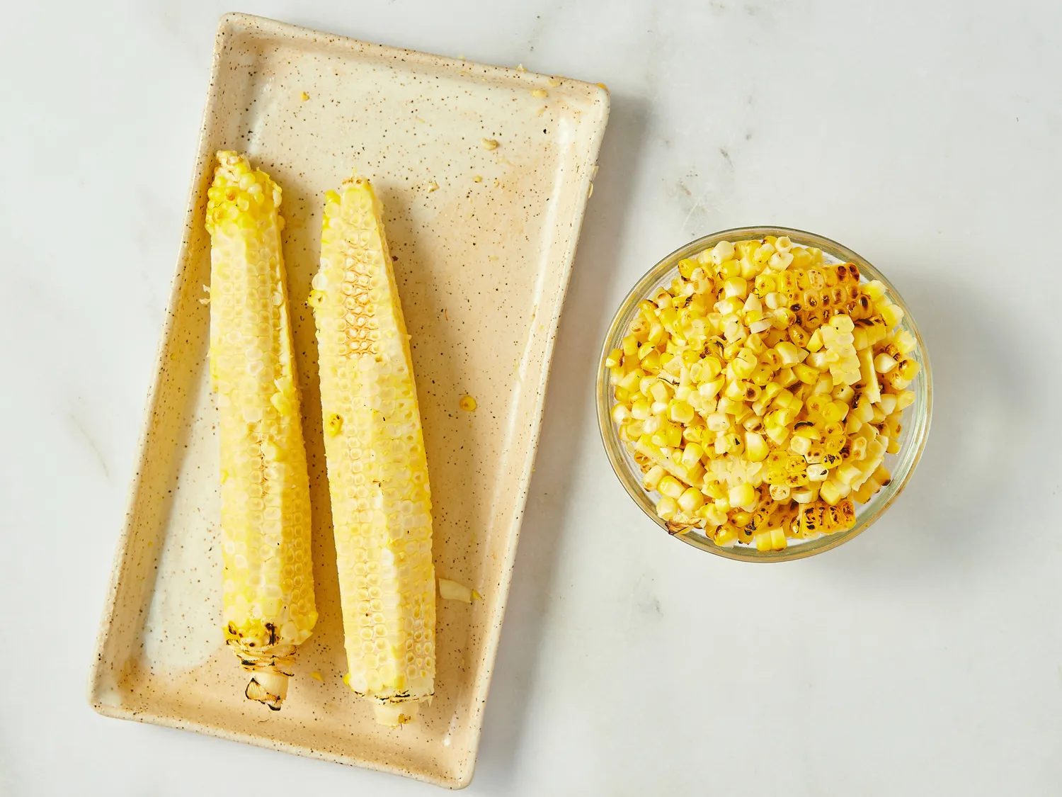 Two corncobs on a plate and a bowl of corn kernels