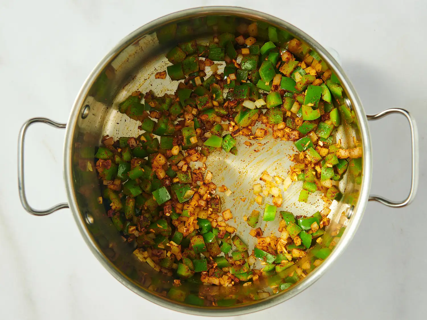 Chopped onions and green bell peppers sautéing in a silver pot