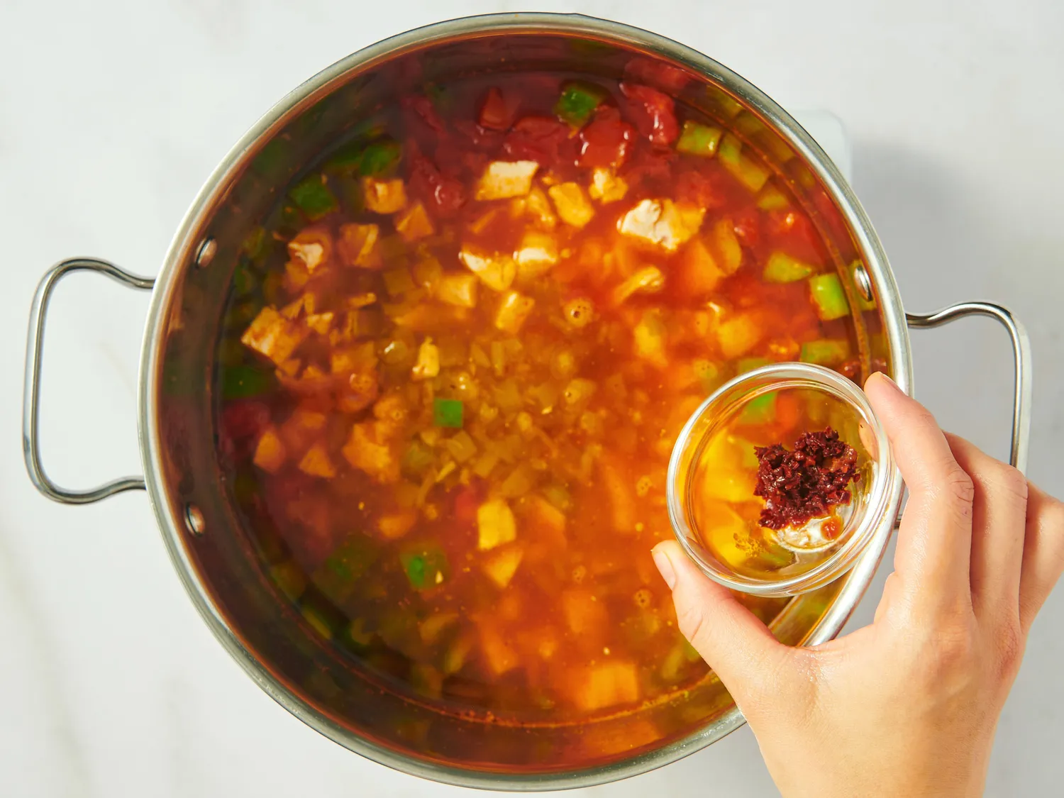A pot of chicken tortilla soup with a hand adding seasoning from a small bowl