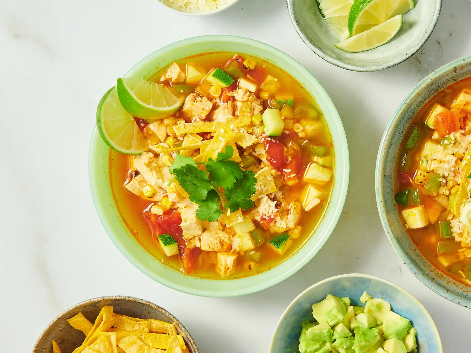 Chicken tortilla soup served with garnishes such as lime, avocado, cheese, and tortilla strips