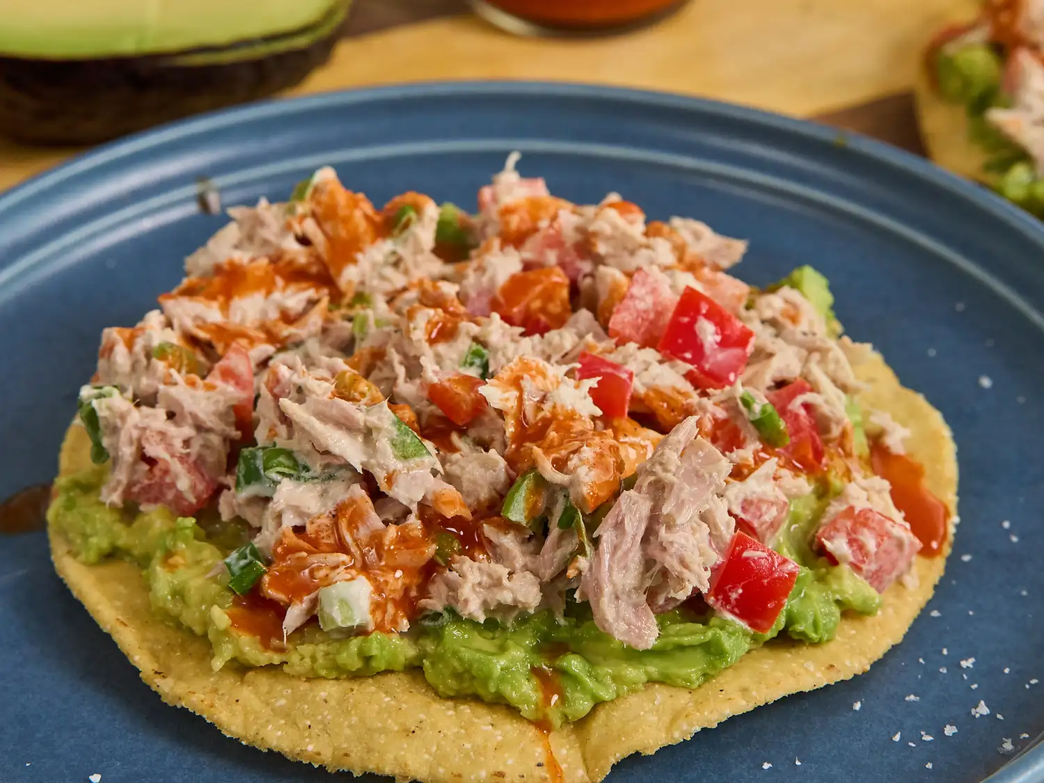 Avocado, tuna salad layered on tostada on blue plate