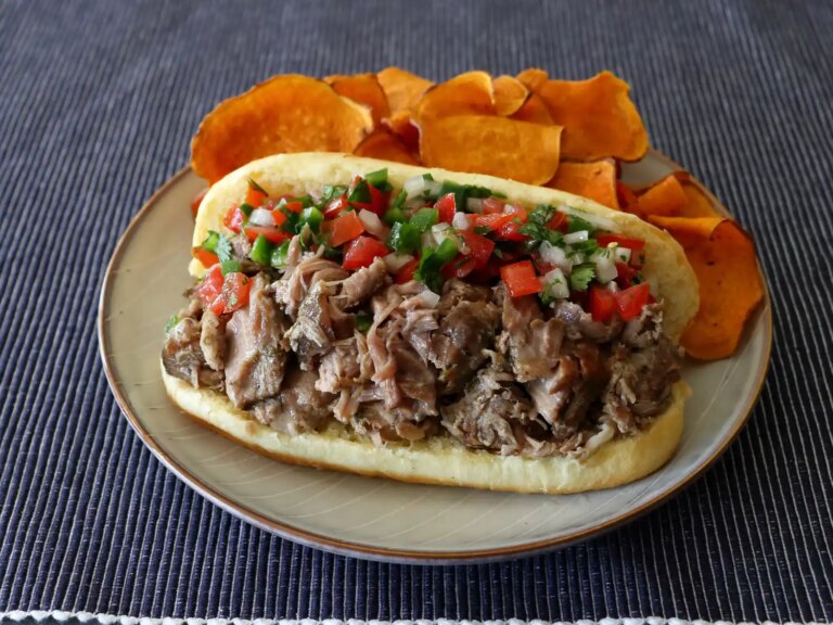 Hot dog bun with campfire carnitas on plate with sweet potato chips