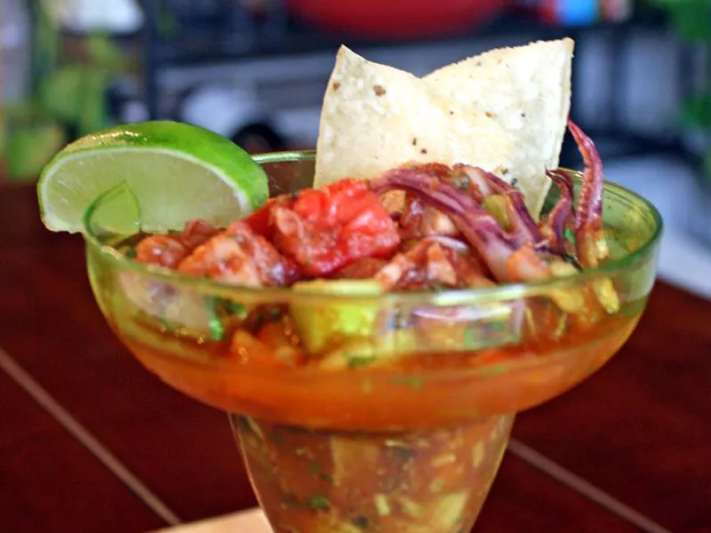 Close up view of juicy and spicy ceviche with squid, ganrished with a lime wedge and tortilla chips in a glass