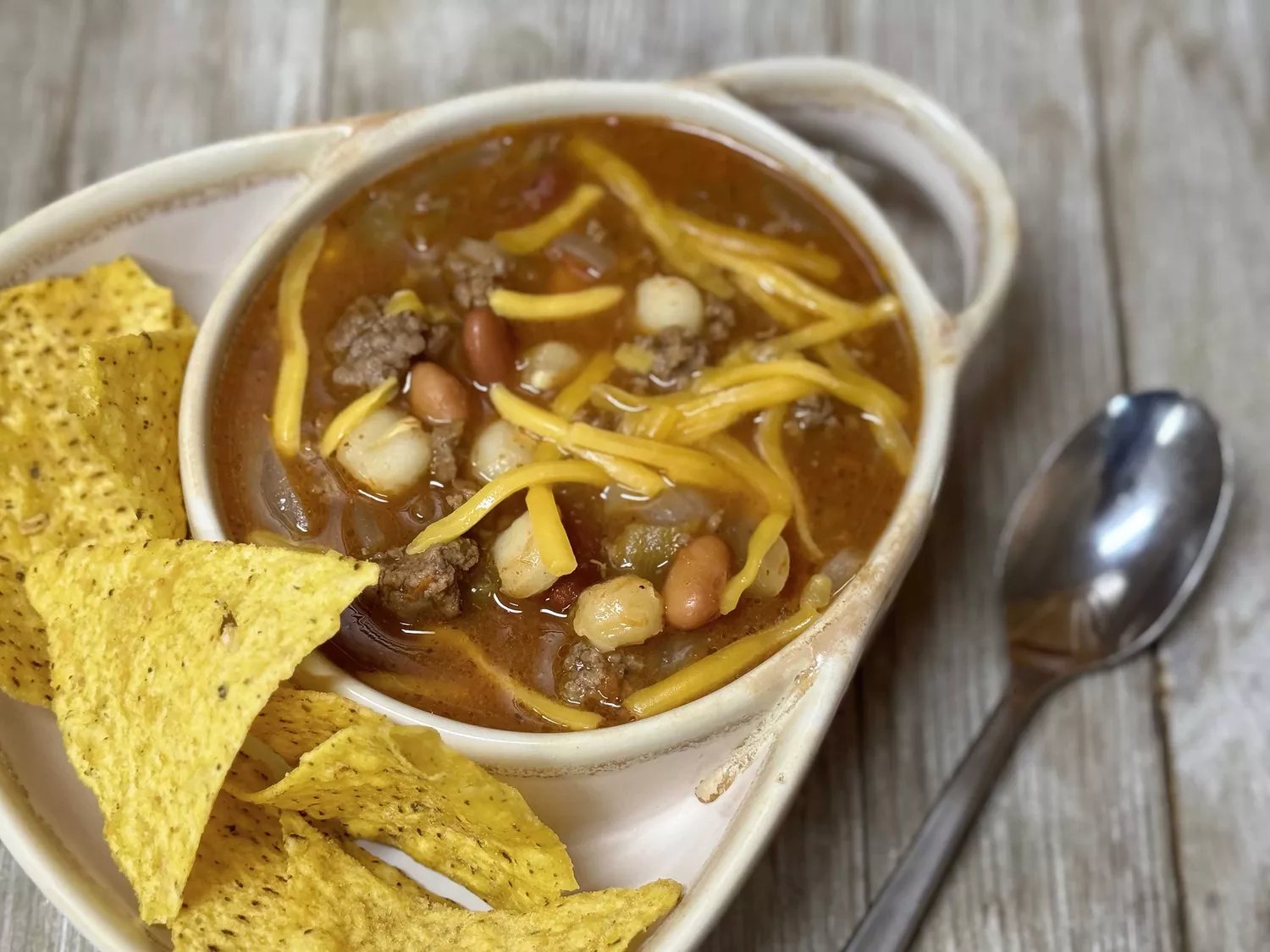 Taco soup topped with cheese and tortilla chips on the side