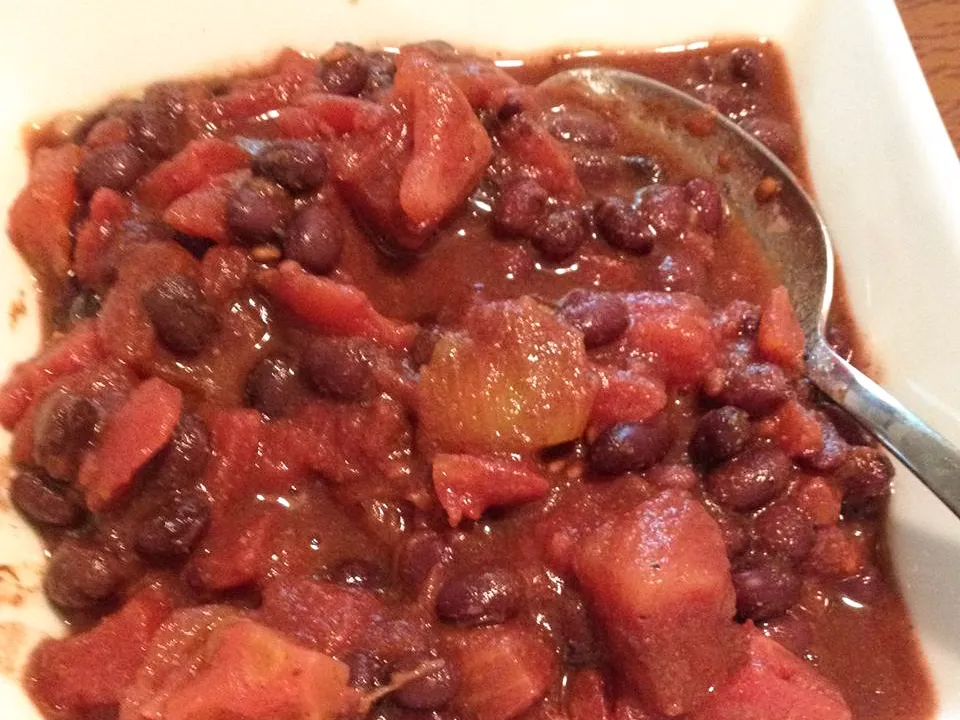 Close up view of black beans and tomatoes in a white bowl with a spoon
