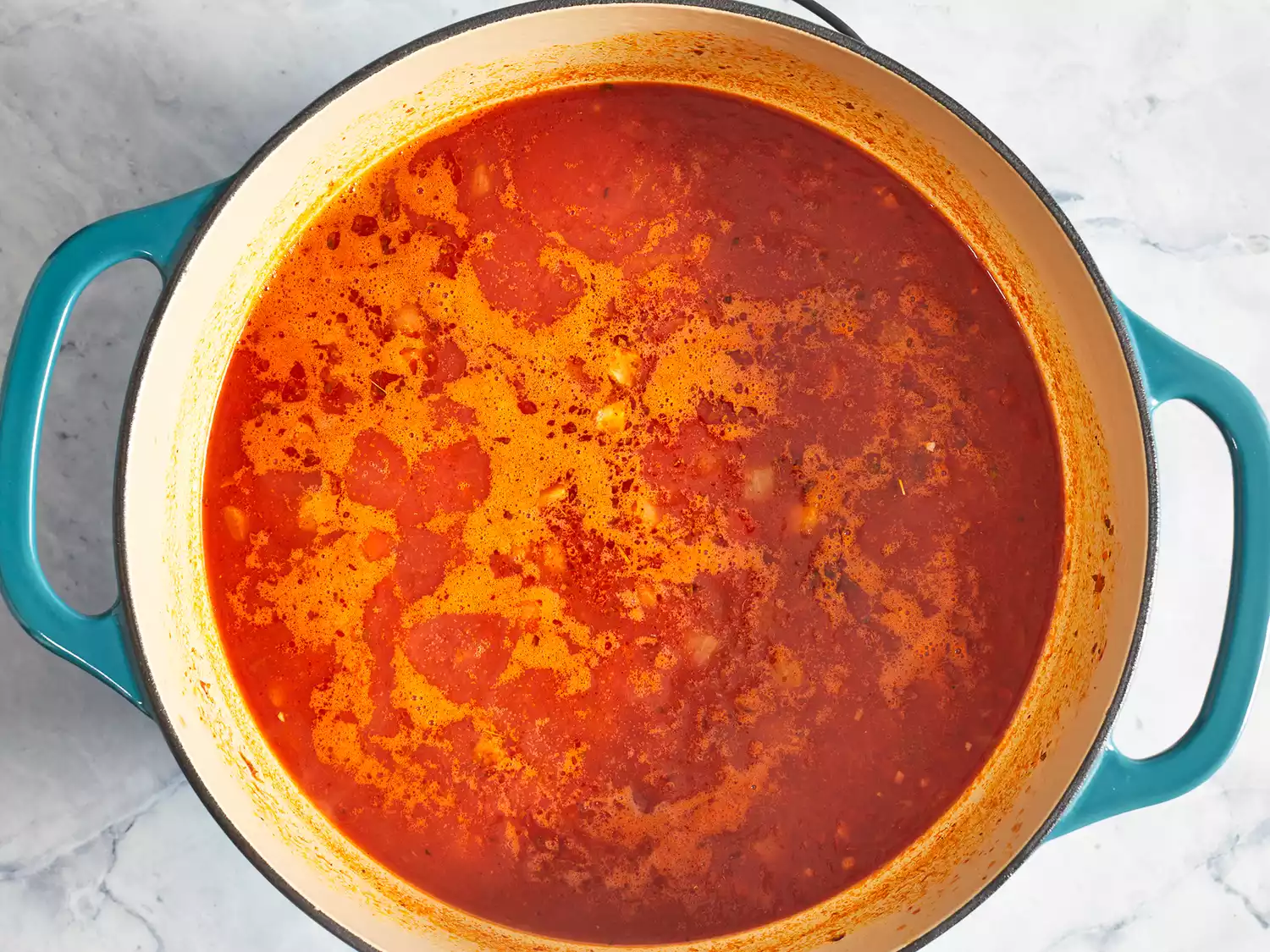 Overhead of crushed tomatos and broth cooking in a large pot. 