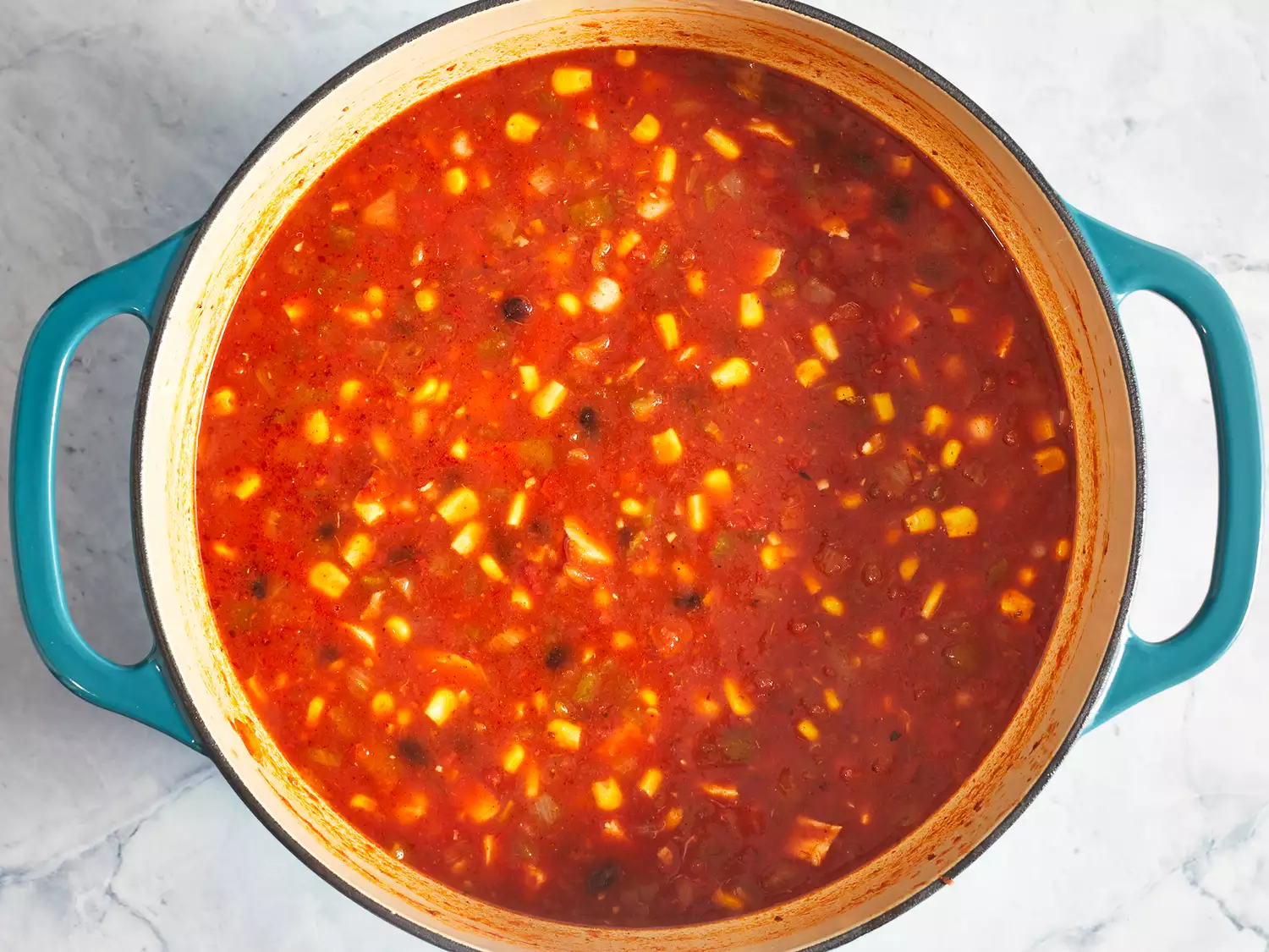 Overhead of black beans, cooked chicken, and corn cooking in a tomato broth in a large pot. 