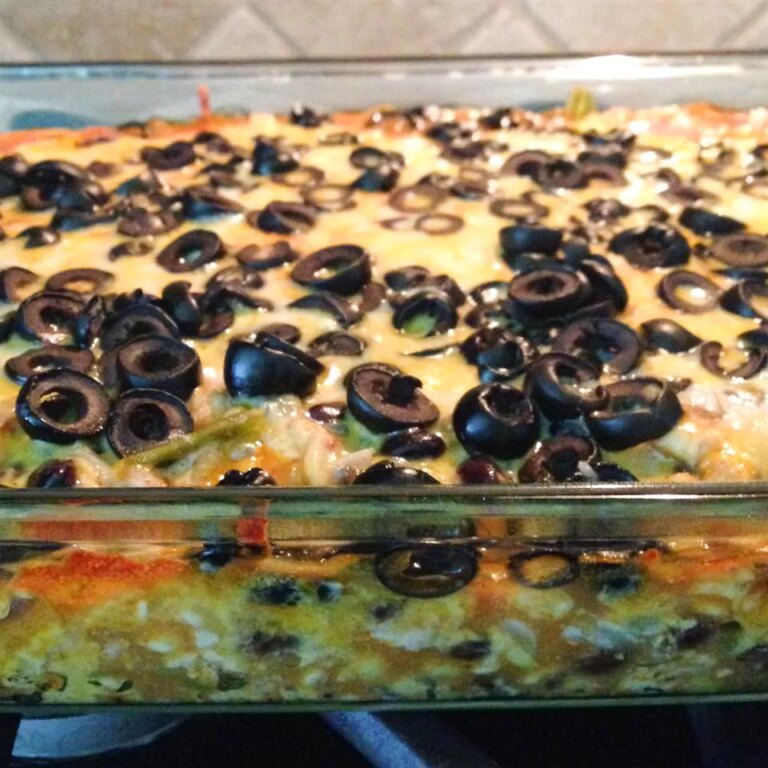 Close up view of enchilada casserole with black olives on top in a glass baking dish