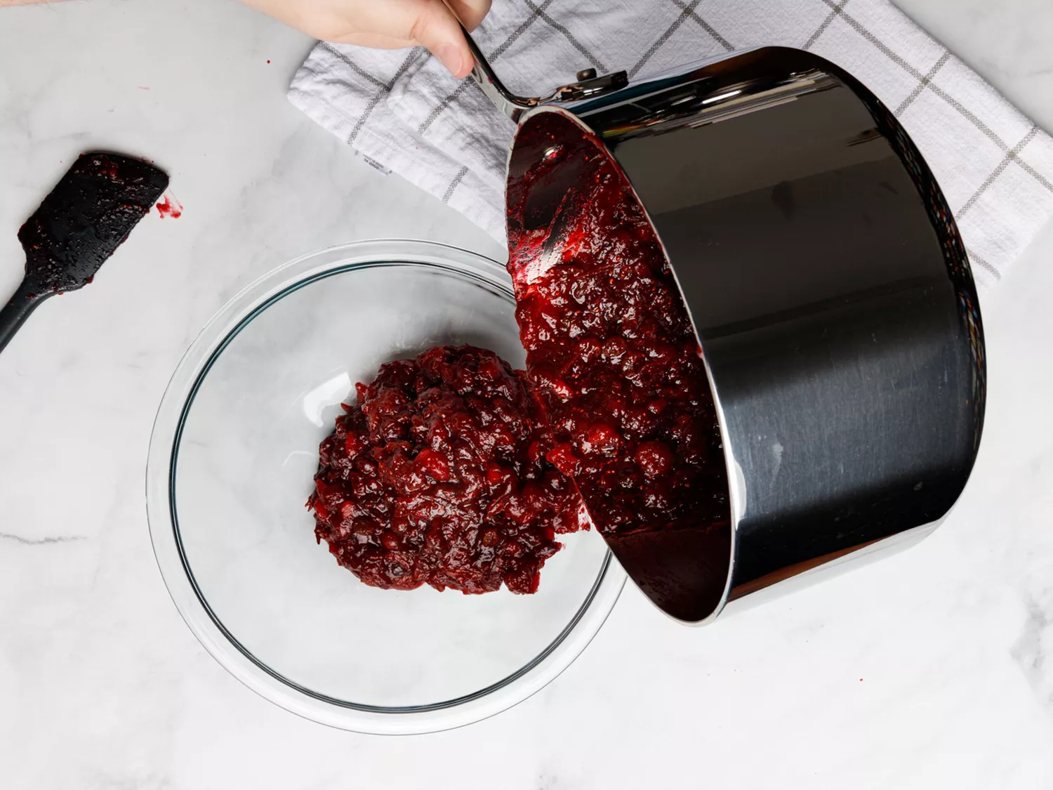 Cranberry chutney getting poured from saucepan into clear mixing bowl